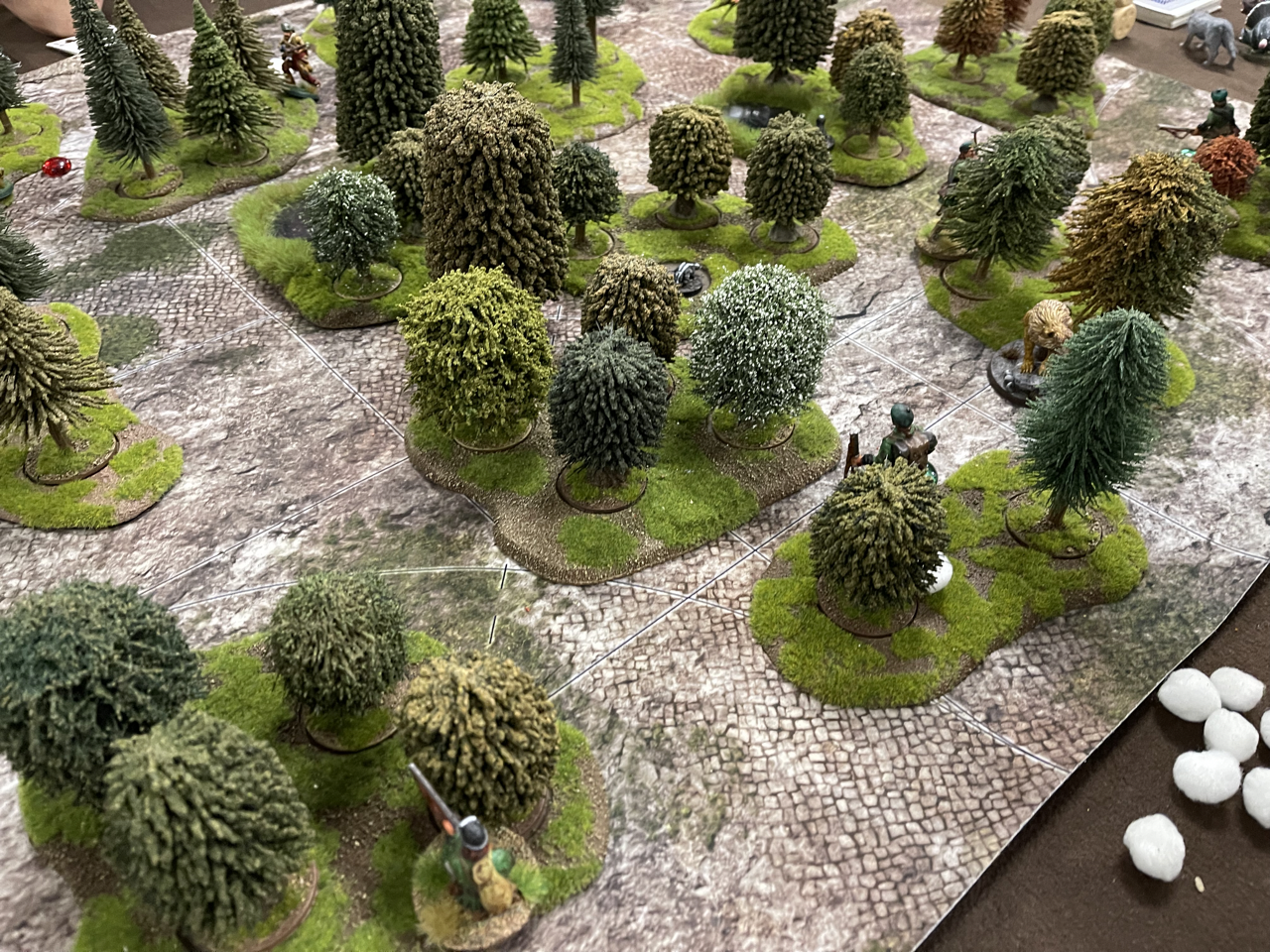 A landscape of miniature trees, with hunter characters hidden in different spots behind them, and white stones. No turkey in sight!